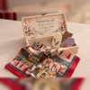 Cutie deschisă: interiorul capacului cu sat de iarnă și mesaj de mulțumire, 3 od Cutie deschisă: interiorul capacului cu sat de iarnă și mesaj de mulțumire, 3 odorizante în cutie și eșarfa pusă peste margine